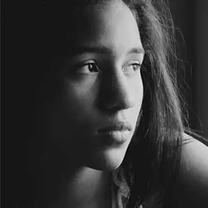 Teen girl gazing thoughtfully out a window, capturing quiet strength and vulnerability.